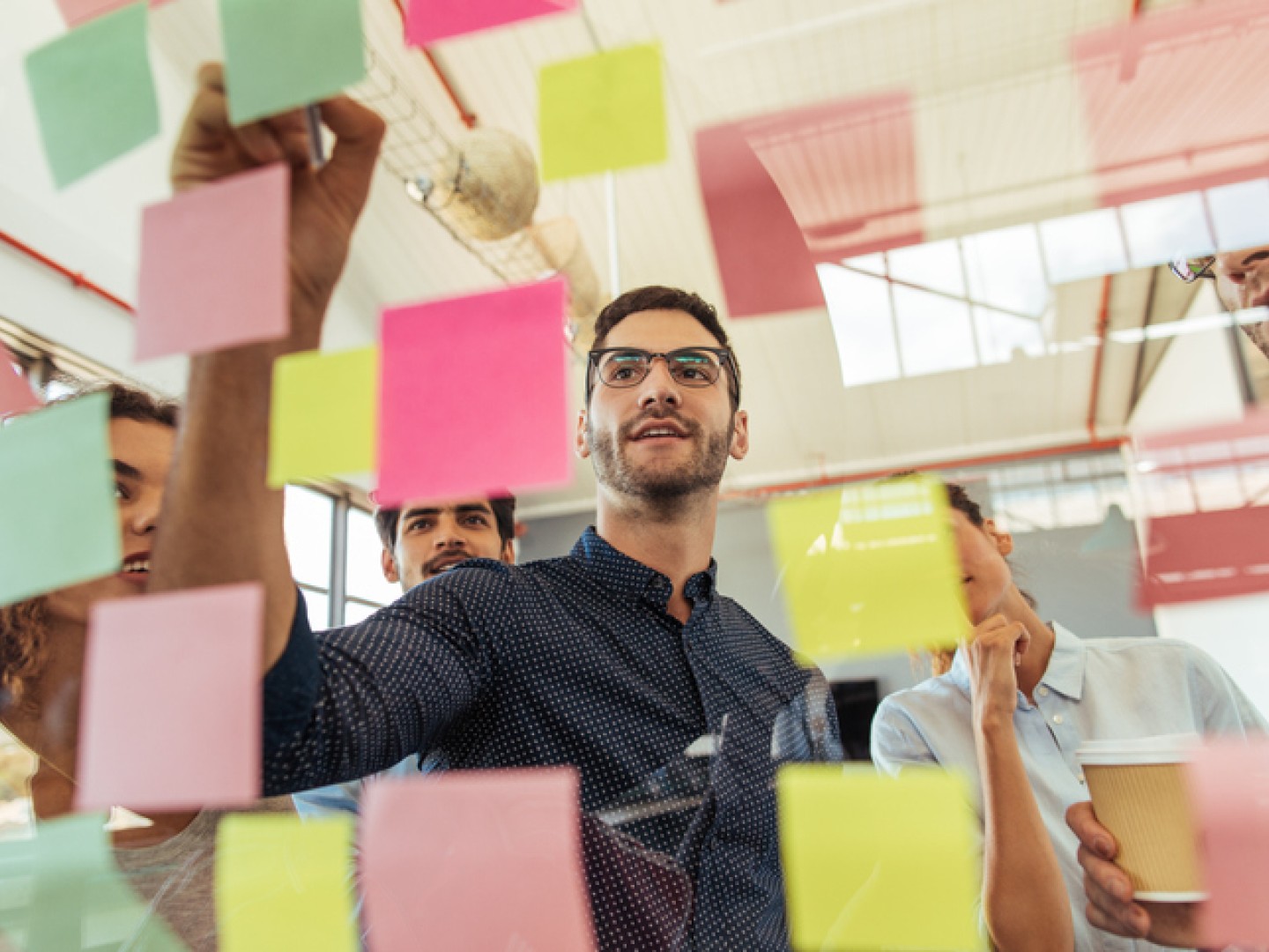 Man taking notes on post-it notes during a brainstorming session with colleagues.