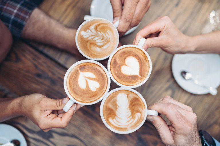 Four hands holding cups of cappuccino viewed from above