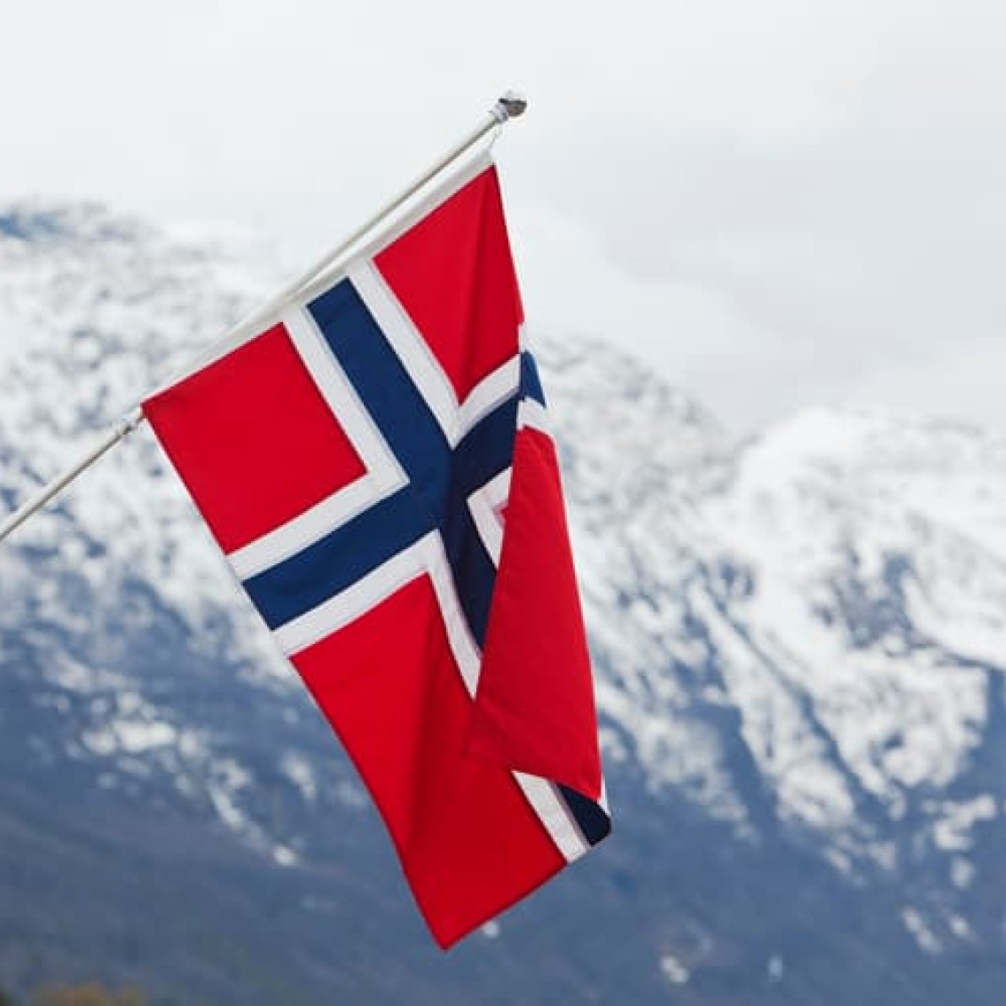 Norwegian flag in red, white and blue with a snow-capped mountain in the background